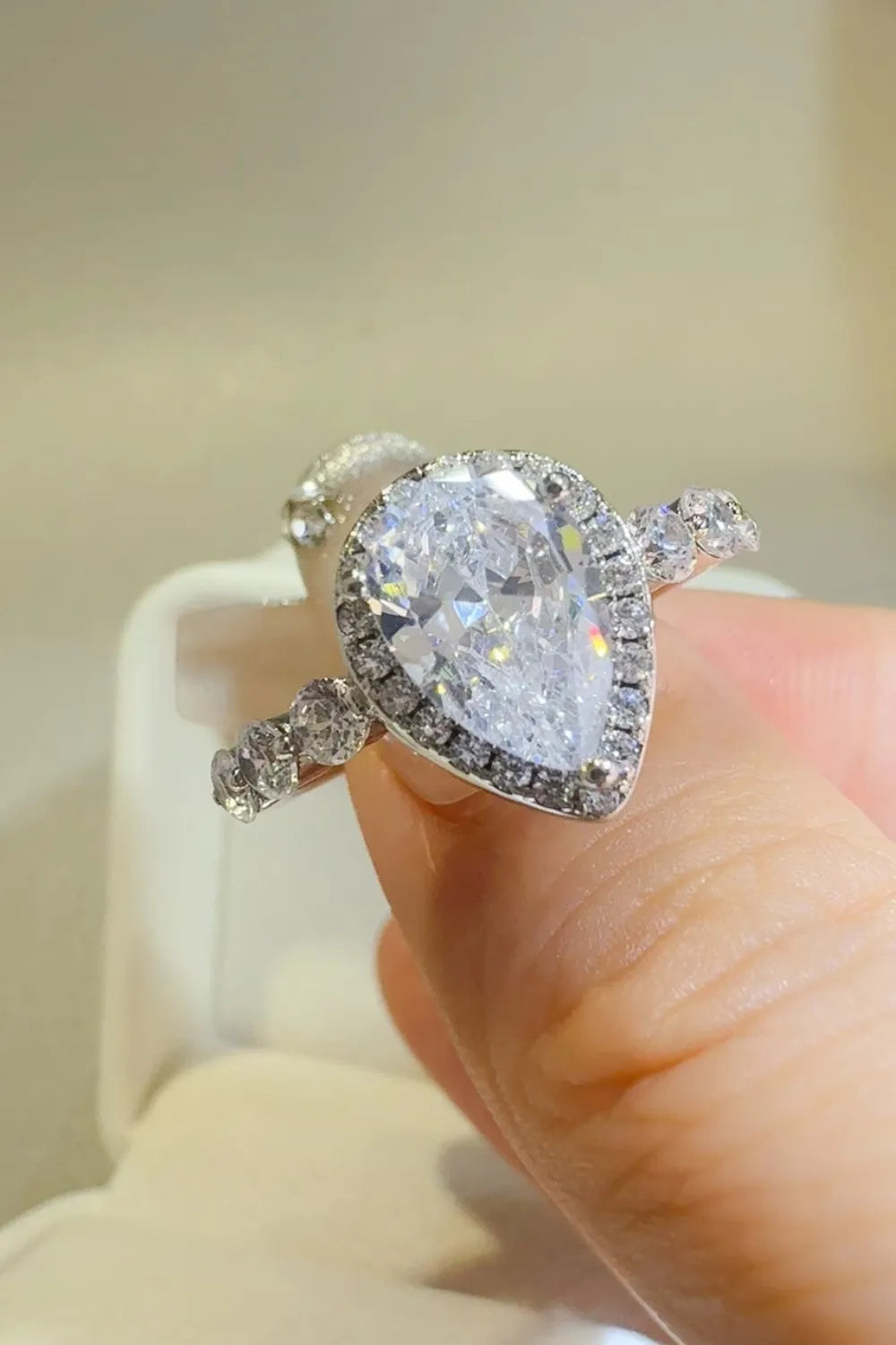 Hand holding a pear-shaped diamond ring with side stones, luxury jewelry at Shopimist