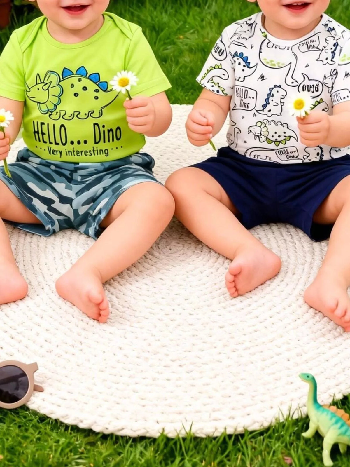 Two toddlers in dinosaur t-shirts sitting on a white mat outdoors, holding daisies, Shopimist kids fashion
