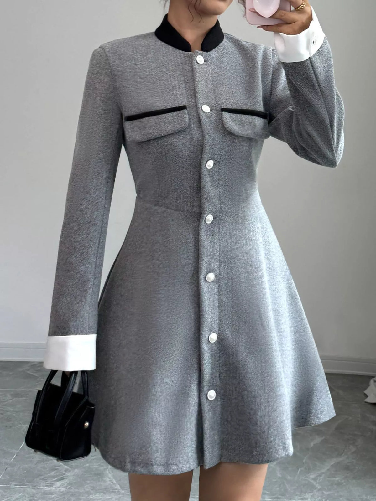 Woman wearing a gray long sleeve button-up dress with black collar, white cuffs, and black handbag, showcasing trendy women's fashion from Shopimist.