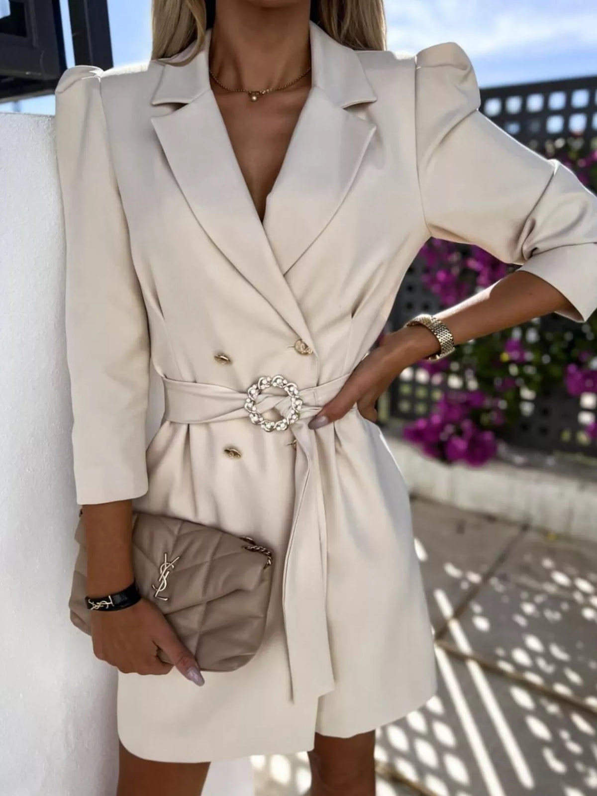 Woman in a belted cream blazer dress holding a quilted beige handbag, stylish summer fashion