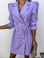 Woman wearing a stylish lavender blazer dress with gold buttons and belted waist, holding a beige purse