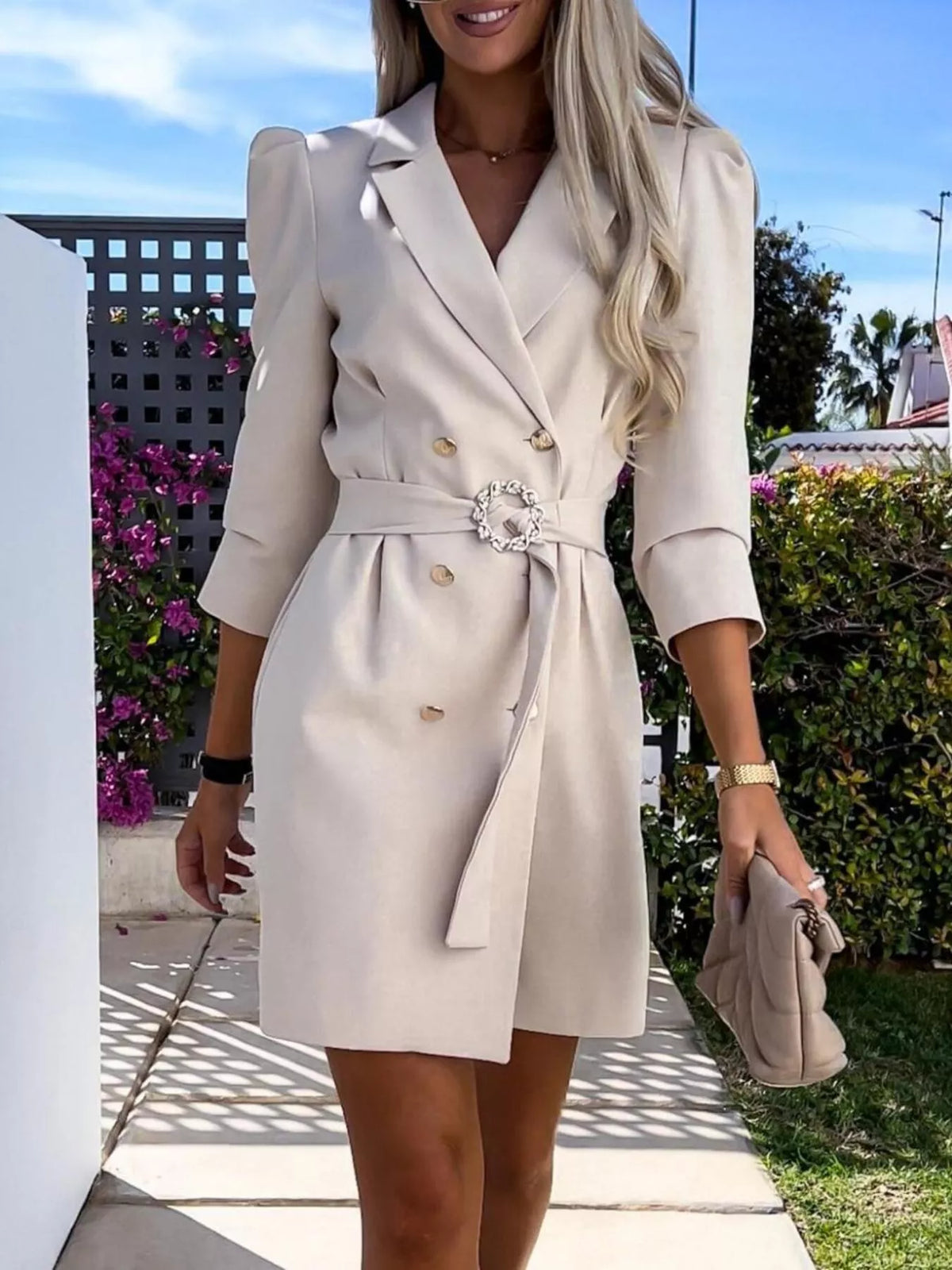 Woman wearing stylish beige blazer dress and holding a quilted clutch outdoors