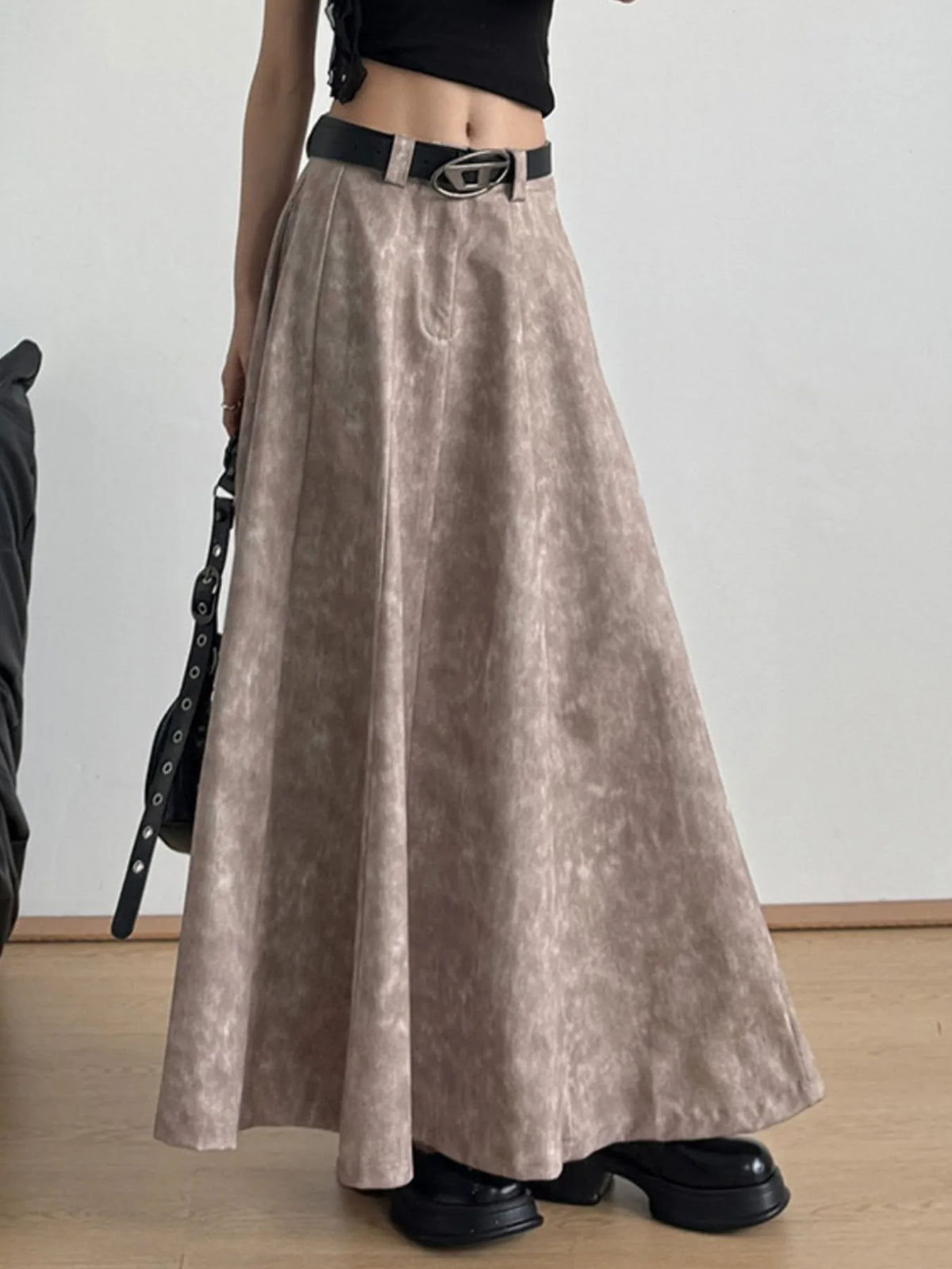Woman wearing a beige maxi skirt with black belt, black crop top, and chunky black shoes.