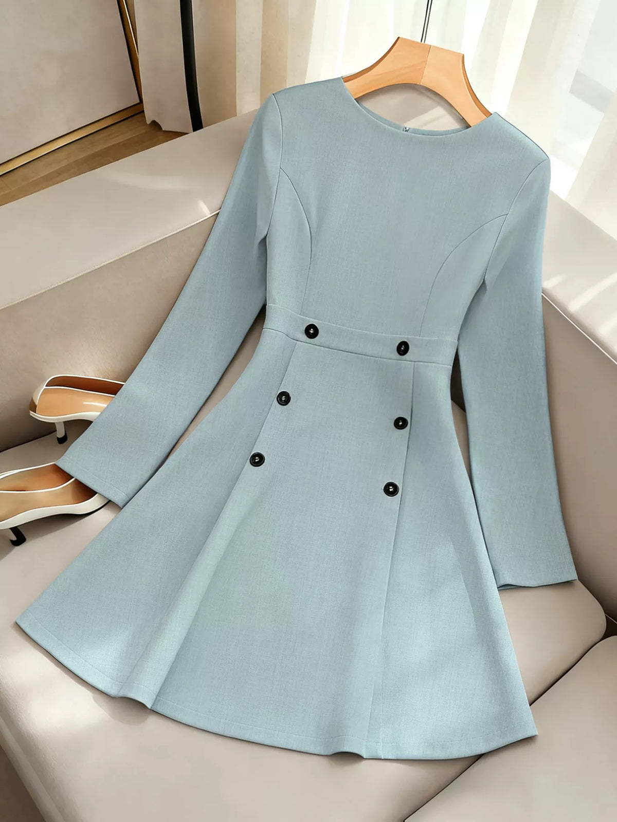 Light blue long sleeve dress with black buttons on a hanger, displayed on a beige sofa, Shopimist fashion