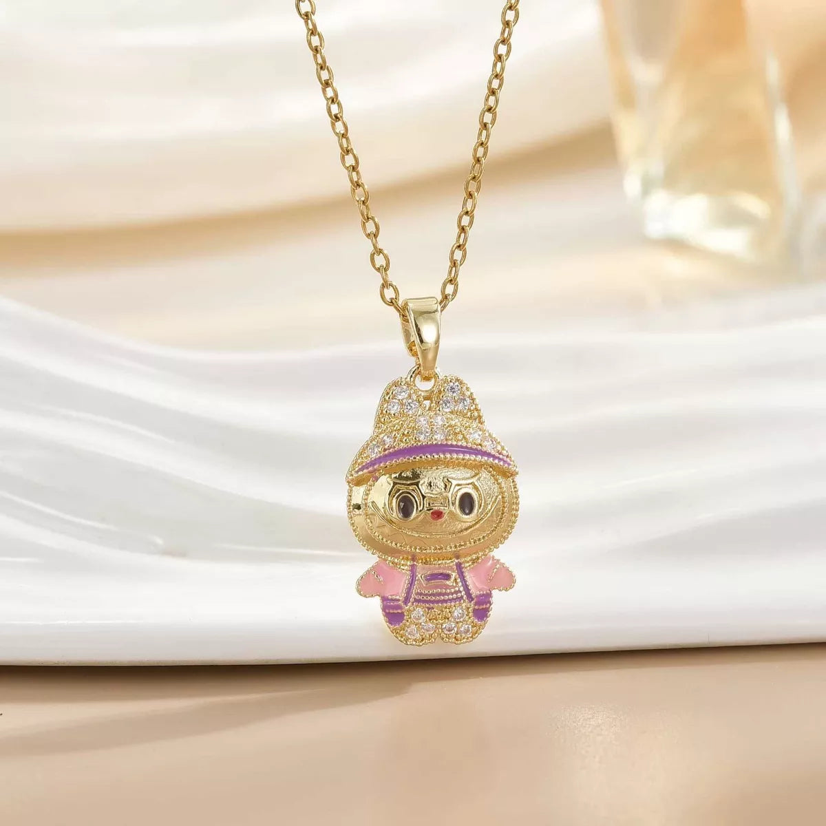 Gold cartoon character pendant necklace with pink and purple details on elegant display