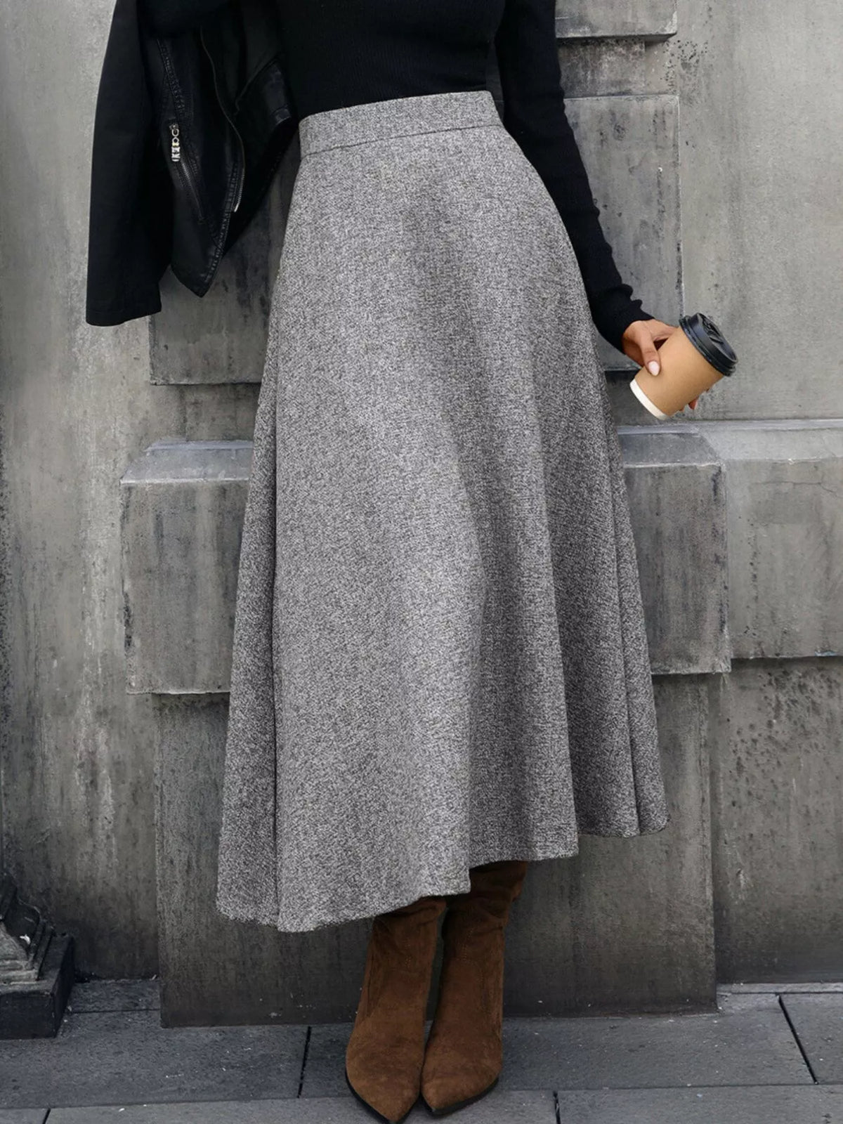 Woman in grey wool midi skirt, black top, brown boots holding coffee, stylish autumn fashion