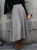 Woman in grey wool midi skirt, black top, brown boots holding coffee, stylish autumn fashion