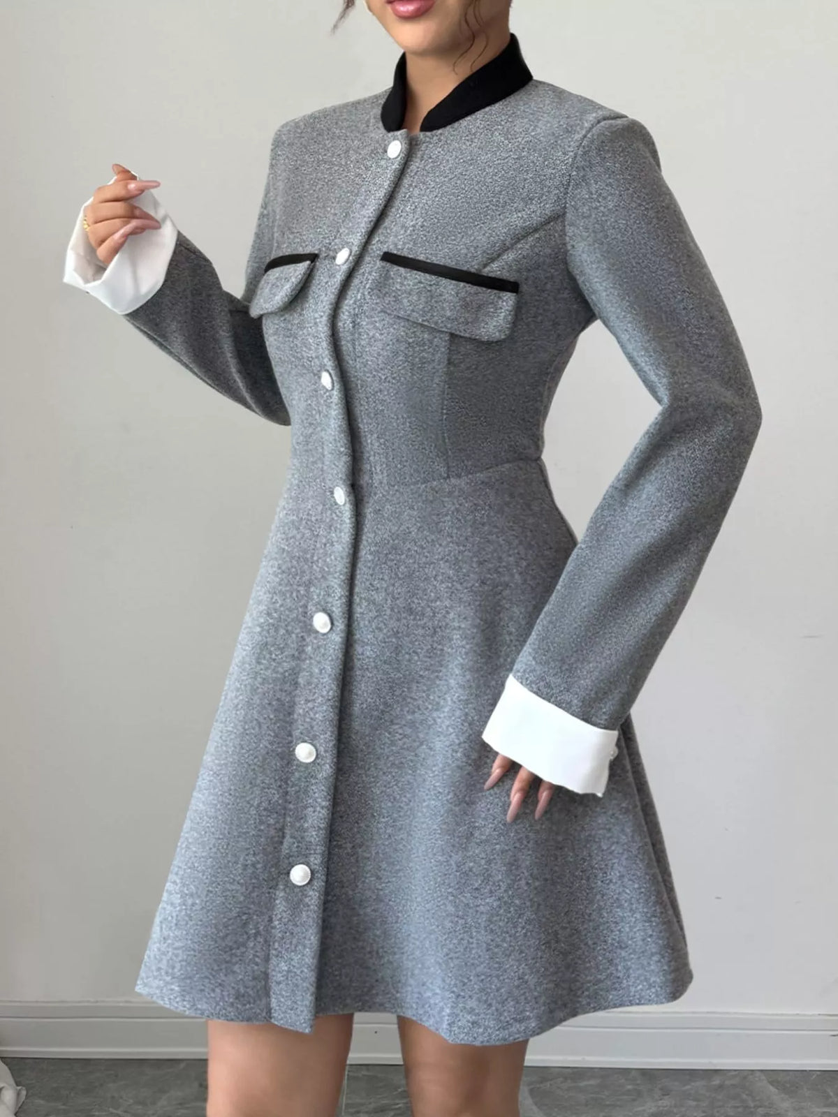 Woman wearing a grey long sleeve button-up dress with black collar, white cuffs, and front pockets.