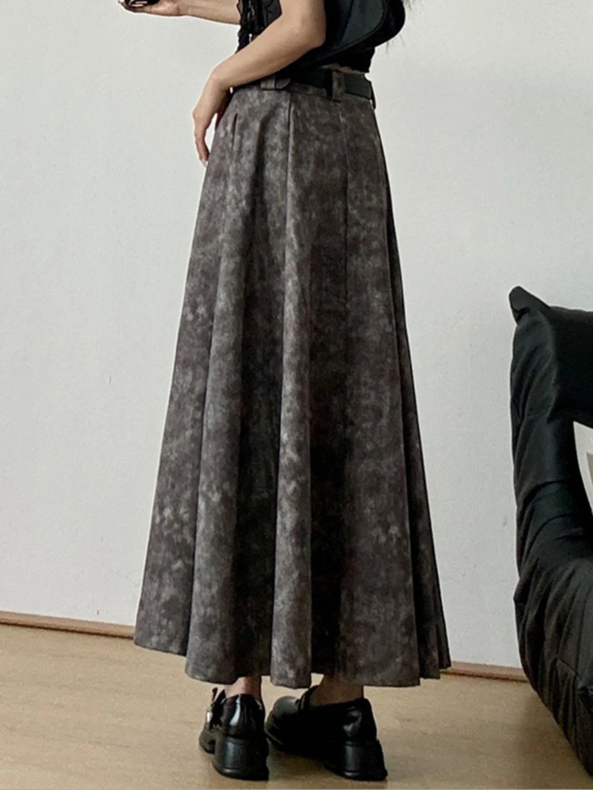 Woman wearing a grey pleated maxi skirt with belt, black shoes, standing indoors