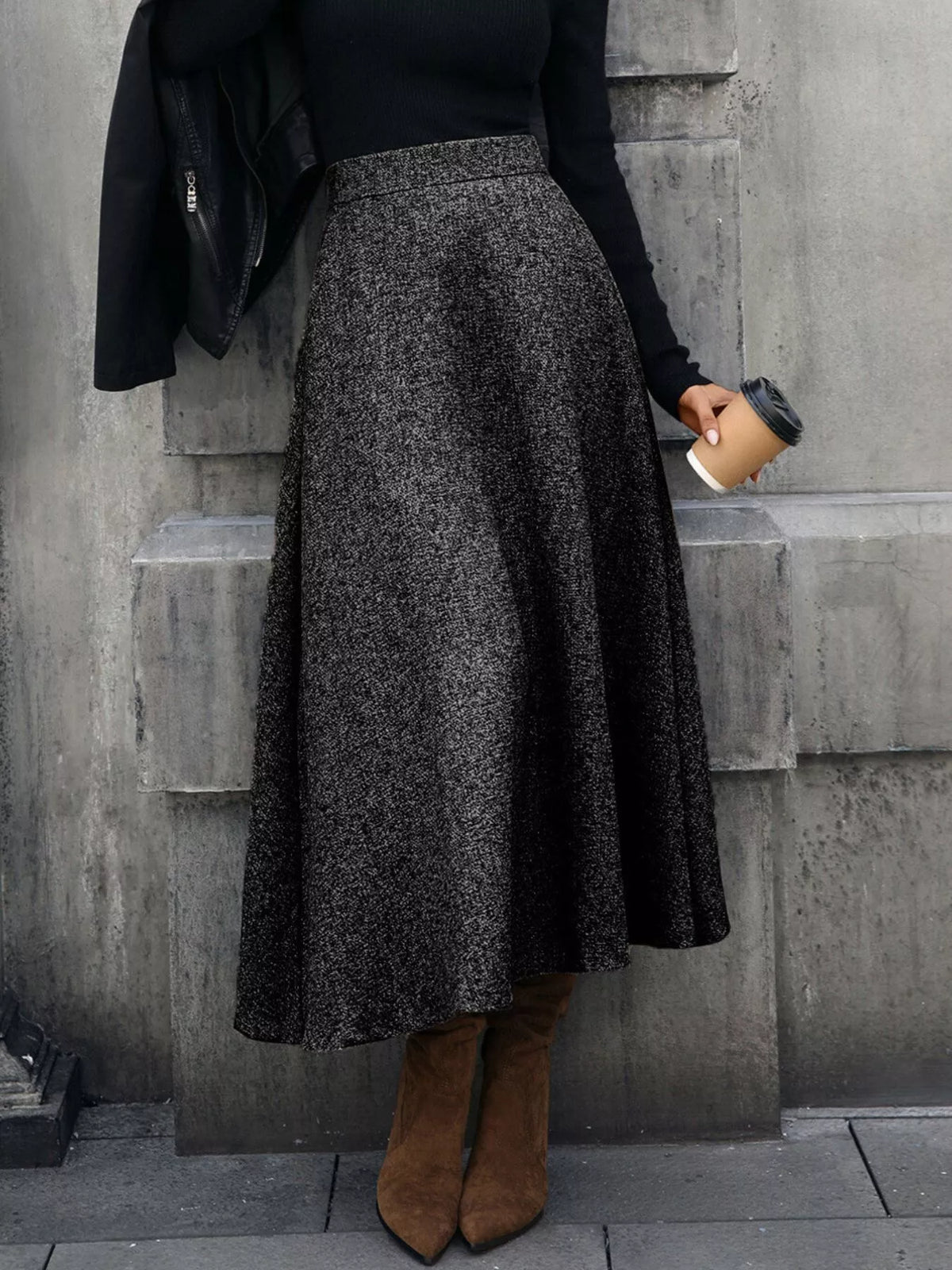 Woman in black sweater and gray maxi skirt with brown boots, holding coffee, stylish street fashion