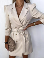 Woman wearing cream blazer dress with belt and gold accessories, holding beige quilted purse