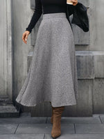Woman in grey wool midi skirt, black top, and brown boots, holding coffee outside, Shopimist fashion