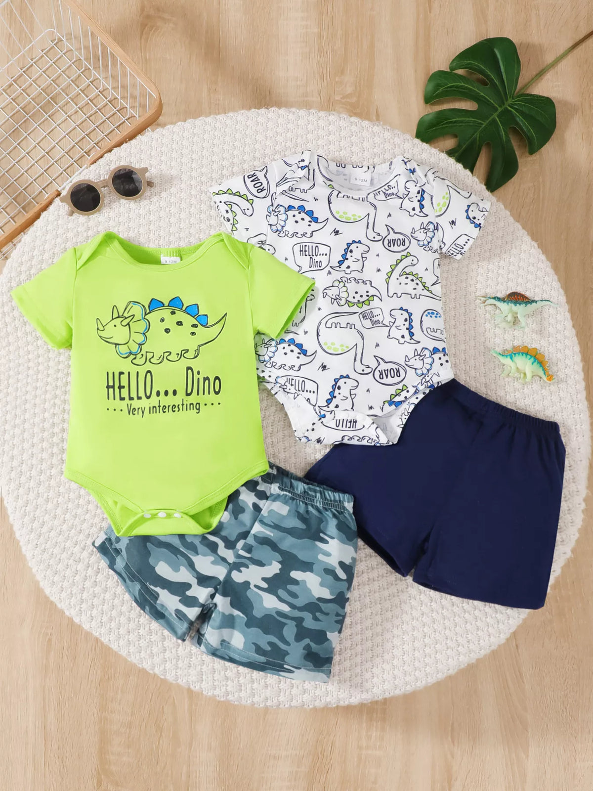 Kids' dinosaur print clothing set with bodysuits, shorts, and toy dinosaurs on wood floor