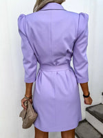 Woman wearing a light purple belted blazer dress holding a taupe clutch, trendy fashion style