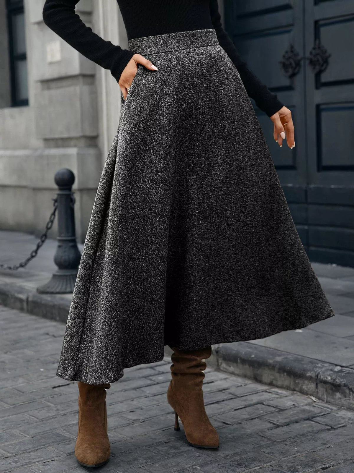Woman wearing a gray wool midi skirt, black sweater, and brown heeled boots on city street