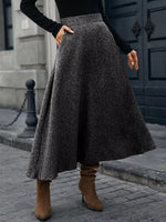 Woman wearing a gray wool midi skirt, black sweater, and brown heeled boots on city street