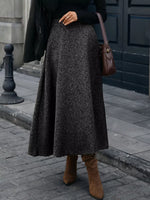 Woman in a black sweater, gray A-line skirt, and brown boots, holding a brown shoulder bag on city street