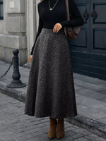 Woman wearing black sweater, grey flared midi skirt, brown boots, and crossbody bag on city street