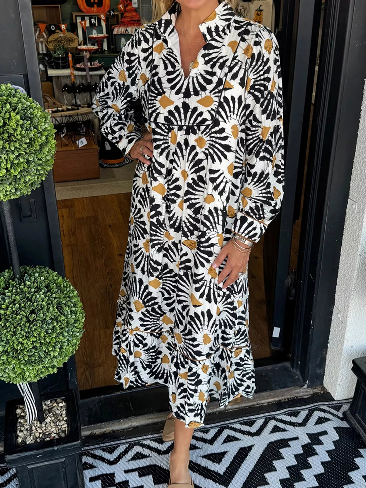 Woman wearing a black and gold floral print midi dress, standing at shop entrance, Shopimist fashion
