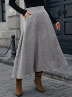 Woman in stylish gray wool midi skirt, black sweater, and brown suede boots on city street